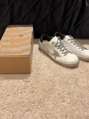 Vita sneakers med grå stjärna - Snygga vita sneakers med grå stjärndetalj på sidan och svarta hälpartier. Skorna har snörning och platt sula. Tillverkade i skinn och har en klassisk, stilren design som passar till det mesta.