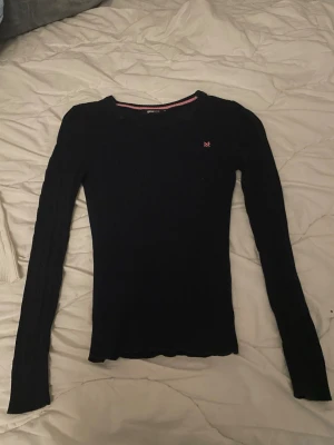 Mörkblå kabelstickad tröja Gina Tricot - Snygg mörkblå kabelstickad tröja från Gina Tricot med rund halsringning och rosa broderad logga på bröstet. Tröjan har långa ärmar och ribbade muddar. Perfekt för dig som gillar klassisk och enkel stil. Använd fåtal gånger 