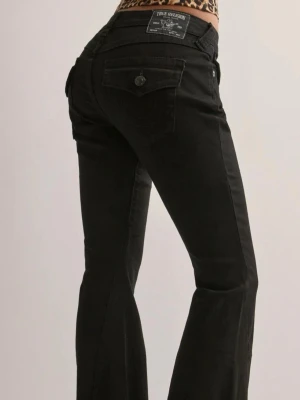 Svarta bootcut jeans från True Religion Joey - Snygga svarta jeans från True Religion med bootcut passform och väldigt låg midja. I modellen ”JOEY”. Som nya då de bara använts en gång. Säljer pga kommer inte till användning, då jag har andra jeans jag föredrar mer. Jeansen är i storlek W25.