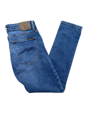 Blå jeans från Nudie Jeans - Snygga blå jeans från Nudie Jeans med klassisk femficksdesign och ikonisk vågsöm på bakfickan. Jeansen har normal passform och raka ben, tillverkade i mjuk bomullsdenim. Perfekta för en avslappnad och stilren look.