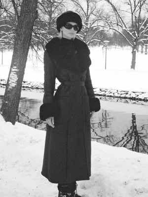 NA-KD x Lovisa Worge kappa - Snygg lång svart kappa med bred pälskrage och pälskanter vid ärmsluten. Jackan har markerad midja med bälte och knappar framtill. Perfekt för kalla dagar när du vill vara både varm och stilren.