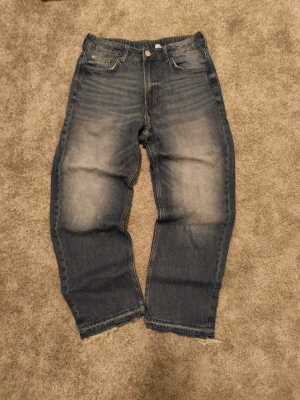 Blå raka jeans med rå kant - Säljer ett par blå jeans som är lite hemma gjorda från hm. Jag har gjort en liten flared look för stilen och brs passform och snyggt slitna detaljer på framsidan. Jeansen har råa, fransiga benslut och klassisk femficksdesign. Perfekta för en avslappnad och trendig look.