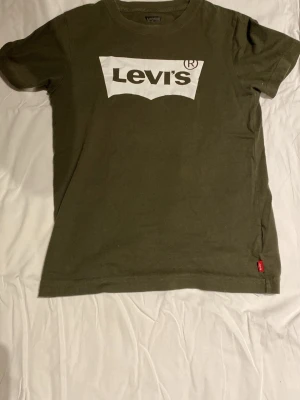 Olivgrön Levi's t-shirt med logga - Snygg olivgrön t-shirt från Levi's med klassisk vit logga framtill. T-shirten har korta ärmar och rund halsringning. Tillverkad i mjuk bomull som känns skön mot huden. Perfekt för en avslappnad och trendig look.