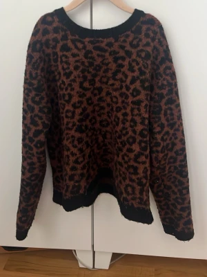 Leopardmönstrad stickad tröja - Stickad tröja med leopardmönster i brunt och svart. Tröjan har rund halsringning, långa ärmar och svarta ribbade muddar vid hals, ärmslut och nederkant. Perfekt för dig som vill ha en trendig och djurinspirerad look.