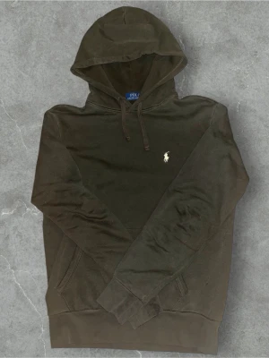Olivgrön hoodie från Polo Ralph Lauren - Polo Ralph Lauren Hoodie – Grön | Strl S  Snygg och klassisk Polo Ralph Lauren hoodie i mörkgrön färg. Broderad vit logga på bröstet. Mjuk och skön kvalitet, perfekt till vardags.  🔹 Storlek: S   🔹 Passform: True to size   🔹 Skick: Den är som ny eftersom jag fick den i julklapp och har knappt använt den! 🔹 Färg: Mörkgrön/Brun  Perfekt basic hoodie som funkar året runt.   Skickas snabbt 📦 — hör av dig vid frågor!