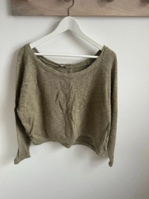 Olivgrön stickad croppad tröja - Säljer en olivgrön stickad tröja med croppad passform och bred halsringning. Tröjan har långa ärmar och är tillverkad i ett mjukt, grovt stickat material. Perfekt för lager på lager och en avslappnad stil.