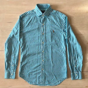 Blårutig skjorta från Polo Ralph Lauren - Snygg blårutig skjorta från Polo Ralph Lauren i slim fit. Skjortan har klassisk krage, långa ärmar och knappar hela vägen. Materialet är mjuk bomull och på bröstet finns den ikoniska broderade Polo-loggan. Perfekt för dig som gillar stilrena och fräscha plagg.