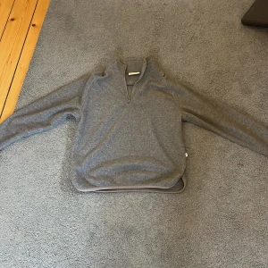 Grå half zip tröja från Grunt - Mysig grå långärmad tröja från Grunt i storlek M. Tröjan har en half zip-dragkedja vid halsen och är tillverkad i ett mjukt stickat material. Perfekt för kyliga dagar och enkel att matcha med jeans eller mjukisbyxor. Jätte bra bas lager både ute i naturen även dagligen i skolan eller med kompisar väldigt all around tröja