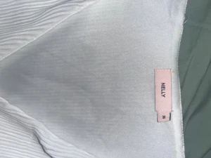 Vit kortklänning med volanger från Nelly - Supersöt vit kortklänning från Nelly med plisserat tyg och volangdetaljer. Klänningen har långärmade ärmar och v-ringad hals. Perfekt för dig som gillar en feminin och fräsch look. Materialet känns lätt och luftigt, vilket gör den skön att bära under varma dagar.