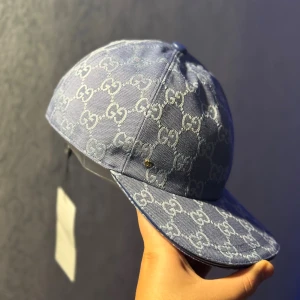 Blå keps från Gucci med GG-mönster - Säljer en blå keps från Gucci med ikoniskt GG-mönster i ljusare blått över hela kepsen. Kepsen har böjd skärm, justerbar rem bak och är tillverkad i bomullsmaterial. Perfekt för dig som vill sticka ut med en lyxig och trendig accessoar.