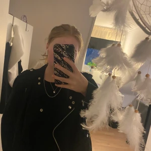 Svart bikerjacka med dragkedjor - Säljer en svart bikerjacka med silvriga dragkedjor och knappar. Jackan har klassisk sned dragkedja framtill, detaljer vid axlarna och dragkedjor vid ärmsluten. Lite knopprig men inget man märker.                                   Skicka för flera bilder eller frågor💕