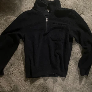 Svart fleece-tröja med half zip - Mysig svart fleece-tröja i storlek S med half zip och hög krage. Tröjan har en bröstficka och är tillverkad i mjukt, fluffigt fleecematerial som håller dig varm. Perfekt för kyliga dagar och chill hemma. Långärmad och enkel att matcha med jeans eller mjukisbyxor. Nypris - 699kr