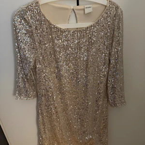 Glittrig trekvart ärmad klänning  - En supersnygg glittrigkläning med champagnefärg från Studio i storlek S. Klänningen har rund hals, trekvartsärm och en snygg öppning i ryggen. Perfekt för dig som vill sticka ut med en glam look. Säljer då jag aldrig använt denna! Så är gott som ny💕