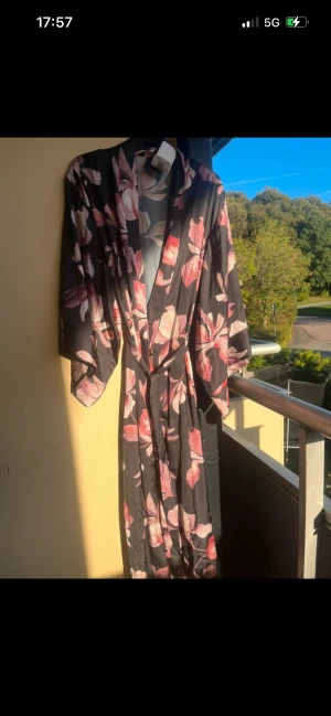 Svart kimono med blommigt mönster - Säljer en svart kimono med rosa och beige blommigt mönster.  Storlek M/L men passar även en S då den går att knyta. Prislappen är kvar ny pris är 599kr 