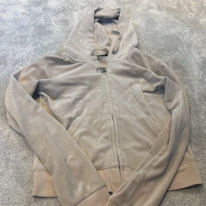Beige hoodie från Juicy Couture S - Säljer en beige hoodie från Juicy Couture i mjuk velour med huva och dragkedja med J-detalj. Tröjan har långa ärmar, ribbade muddar och fickor framtill. Perfekt för chill dagar och har en snygg, klassisk look.