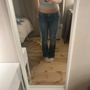 Blå bootcut jeans från Levi's - Säljer ett par klassiska blå jeans bootcut passform och låg midja. Jeansen har, fem fickor och knappgylf. Perfekt för dig som gillar en tidlös och avslappnad stil.