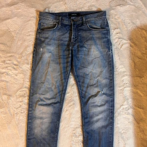 Blå jeans från J.Lindeberg - Snygga blå jeans från J.Lindeberg med klassisk femficksdesign och slitningar på benen. Jeansen har en rak passform och är tillverkade i mjukt denimtyg. Perfekta för dig som gillar en avslappnad och stilren look.
