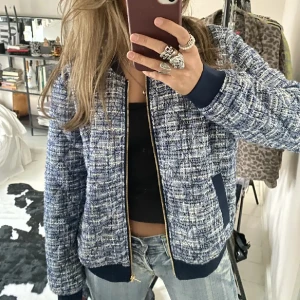 Blåvit bomberjacka med dragkedja - Säljer en snygg blåvit bomberjacka med grovt vävt tyg och mörkblå muddar vid ärmslut och nederkant. Jackan har guldfärgad dragkedja och två fickor fram. Perfekt för dig som gillar en chill och trendig look. Pris kan diskuteras 