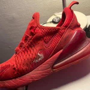 Nike Air 270 röda sneakers - Säljer ett par Nike Air 270 sneakers i helrött med mesh-överdel och synlig Air-sula. Skorna har snörning och en sportig design med rund tå och platt sula. Swoosh-loggan och 270-detaljer på sidan. Perfekt för dig som gillar färgstarka sneakers.