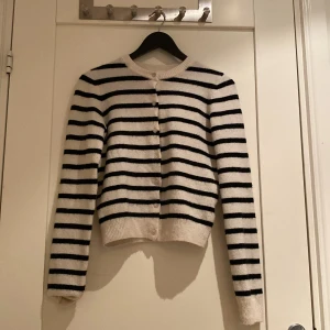 Randig kofta från H&M i XS - Snygg vit och svart randig kofta från H&M i storlek XS. Koftan har rund hals, långa ärmar och knappar framtill. Mjuk stickad känsla som är perfekt för lager-på-lager. Passar dig som gillar klassisk och chill stil.