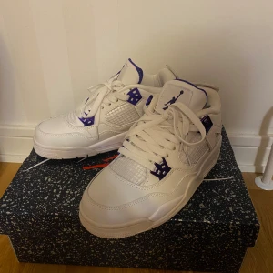  Jordan 4 vit/lila - Jordan 4 sneakers i vitt skinn med lila detaljer och klassisk mesh på sidorna. Perfekta för dig som vill sticka ut med en ikonisk och stilren sneaker.