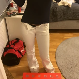 Vita bootcut jeans från Replay - Säljer ett par vita jeans från Replay med bootcut-passform och låg midja. Klassisk femficksmodell med snygga detaljer som Replay-logga på bakfickan och metallmärke. Jeansen är tillverkade i jeansmaterial med dragkedja och knapp framtill. Pris kan diskuteras!