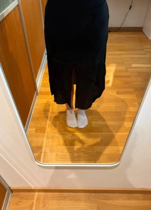 Svart långkjol från Gina Tricot - Svart långkjol från Gina Tricot med elastisk midja och snygga veckade detaljer, med en liten slits framtill. Kjolen har en flowy passform och är tillverkad i ett lätt material som ger en skön känsla. Perfekt för dig som gillar stilrena och enkla plagg med lite extra rörelse.