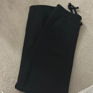 Svarta mjukisbyxor med snörning - Svarta mjukisbyxor med elastisk midja och snörning, samt stora fickor fram. Perfekta för chill dagar och har en loose passform. Materialet känns mjukt och bekvämt mot huden.