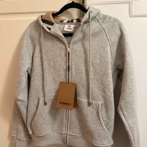 Grå hoodie från Burberry med dragkedja - Snygg grå Burberry hoodie, som tyvärr inte passade mig. Säljer den för väldigt bra pris, ej använd någon gång. OBS pris kan diskuteras!