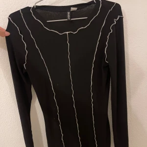 Svart långärmad topp från H&M Divided - Svart långärmad topp från H&M Divided med kontrasterande vita vågiga sömmar längs hela tröjan. Tight passform och stretchigt material som sitter snyggt på kroppen. Perfekt för dig som gillar trendiga detaljer och en clean look.
