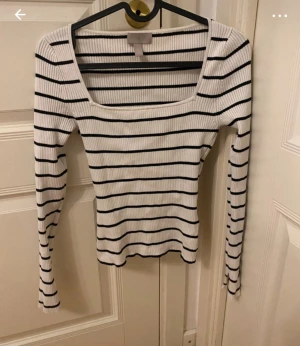 Randig ribbad topp från H&M XS - Säljer en vit och svart långärmad topp från H&M i storlek XS. Toppen är ribbad med smala svarta ränder och har en fyrkantig urringning. Materialet är stretchigt och sitter snyggt figurnära. Perfekt att styla med jeans eller kjol.