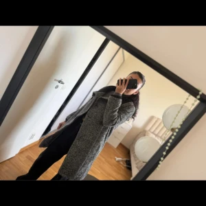 Grå skepparkavaj från Tiger of Sweden - Säljer en grå skepparkavaj från Tiger of Sweden med dubbelknäppning och bred krage i stickad svart material. Jackan har lång ärm och är tillverkad i en grov ullmix som ger en cool och tidlös vibe. Perfekt för dig som gillar klassisk stil med edge.