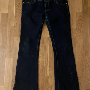 Mörkblå bootcut jeans från Vavell - Snygga mörkblå jeans från Vavell med bootcut passform och klassiska detaljer. Jeansen har kontrastsömmar, fem fickor och dekorativ brodering på fickorna. Tillverkade i jeansmaterial med en skön och normal passform. Perfekt för dig som gillar retrovibbar.