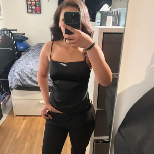 Svart satin linnetopp med rosett - Säljer en svart linnetopp i satin med smala axelband och stor rosett i ryggen. aldrig använd men utan prislapp