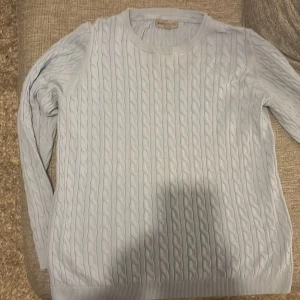 Ljusblå kabelstickad tröja Basic You - Snygg ljusblå kabelstickad tröja från Basic You i storlek L. Tillverkad i mjuk ekologisk bomull med rund hals och långa ärmar. Perfekt för dig som gillar klassisk stil med en modern touch. Ribbad kant vid ärmslut och nederkant.