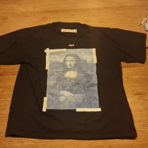 Svart off-white med blå mona lisa bild - Off-white med lite slitet mona lisa märke annars är själva t shirten i bra skick märket där bak är i best skick o skulle sagt att den passar S och M