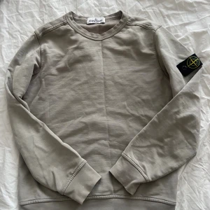 Stone Island junior sweatshirt  - Säljer en stilren beige sweatshirt från Stone Island Junior. Tröjan har rund halsringning, långa ärmar och den klassiska loggan på vänster ärm. Tillverkad i mjuk bomull för en skön och avslappnad känsla.