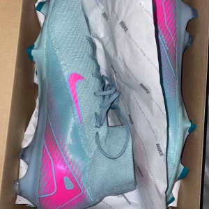 Nike superfly elite 10   - Snygga Nike fotbollsskor i grått med skarpa rosa detaljer och mönster. Skorna har snörning, platt sula med dobbar och en strumpliknande hög krage för extra stöd. Tillverkade i syntetmaterial med Dynamic Fit-teknologi för optimal passform på planen. Fotbollsskorna är en elite modell vilket är proffesionella fotbolls skor. Skorna är äkta och i storlek 47,5. Vid intresse kan kvitto tillhandahållas.