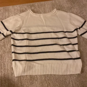 Vit och svart randig stickad tröja - Snygg stickad tröja i vit med svarta horisontella ränder. Tröjan har rund hals och långa ärmar, samt ribbad kant vid nederdelen och ärmsluten. Perfekt för dig som gillar klassisk och enkel stil.