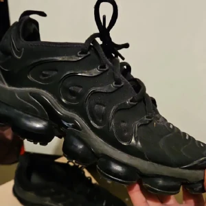 Nike Vapormax svarta sneakers - Svarta Nike Vapormax sneakers med unik bubblig sula och vågiga detaljer på ovansidan. Skorna har snörning och är tillverkade i syntet och textil. Perfekt för dig som gillar futuristisk design och vill sticka ut med dina kicks.