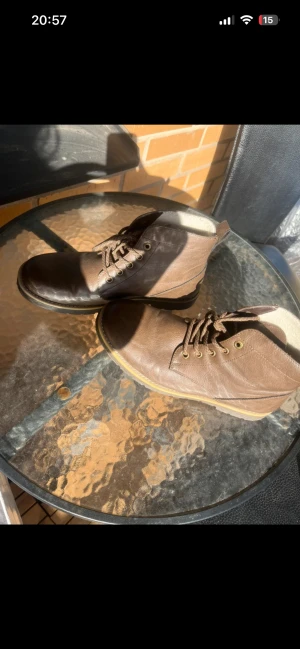 Bruna boots med snörning i skinn - Säljer ett par snygga boots i brunt skinn med snörning och rund tå. Skorna har en platt sula och detaljer i mörkbrunt framtill. Perfekta för dig som gillar klassisk stil med en modern touch. Kvitto finns använda 2-3 gånger 