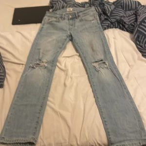 Ljusblå jeans från 157, straight fit - Säljer ett par ljusblå jeans från 157 med straight fit och slitna detaljer vid knäna. Klassisk femficksmodell med dragkedja och knapp. Jeansen har en avslappnad look och är tillverkade i bomull. Perfekt för dig som gillar streetstyle.