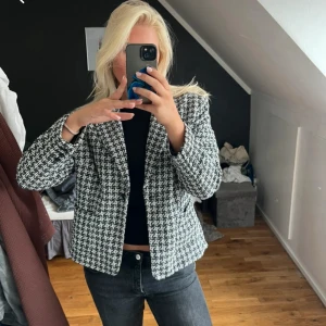 Svartvit rutig kavaj med knappar - Säljer en snygg svartvit kavaj med rutigt mönster och klassisk krage. Kavajen har en knapp framtill och är i en kortare, boxig modell med lång ärm. Perfekt för dig som gillar stilrena och trendiga plagg med lite edge.