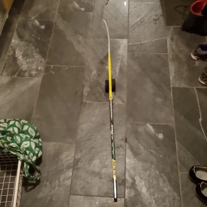 CCM Super Tacks Ishockeyklubba - CCM Super Tacks ishockeyklubba i barn/yth stolek, med tydlig märkning och färg. Klubban har gul/grön design. Klubban ser ut att vara i lite slitet skick med mindre tecken på användning. Perfekt för både träning och match.