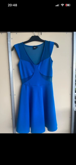 Blå kortklänning från ASOS - Snygg blå klänning från ASOS med v-ringad hals och meshdetaljer vid axlar och midja. Klänningen är ärmlös och har en utställd kjol som ger en ungdomlig och fräsch look. Perfekt för dig som vill sticka ut med färg och stil. Använd 1 gång 