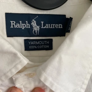 Vit skjorta från Ralph Lauren - Klassisk vit skjorta från Ralph Lauren med broderad polospelare på bröstet. Modellen Yarmouth är tillverkad i 100% bomull och har lång ärm, knappar framtill och krage. Perfekt för dig som gillar stilrena och tidlösa plagg med snygga detaljer.