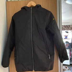 Svart vindjacka från Barbour XL - Svart vindjacka från Barbour International i storlek XL i barn storlek. Men sitter som xs Jackan har huva, två fickor med dragkedja och hel dragkedja framtill. Stilren design med Barbour-logga på ärmen. Perfekt för blåsiga dagar och enkel att matcha med din outfit.