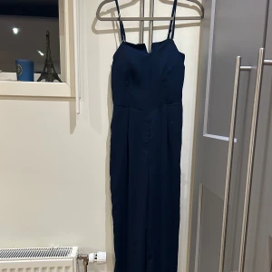 Marinblå byxdress med fickor - Snygg marinblå byxdress med smala justerbara axelband och smockad rygg för extra komfort. Den har en rak siluett och praktiska fickor i sidorna. Dragkedjan har hoppat ur där av lägre pris