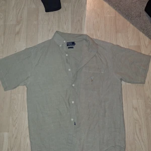 Beige kortärmad skjorta Polo Ralph Lauren - Snygg beige skjorta från Polo Ralph Lauren i 100% bomull. Klassisk passform med korta ärmar, knappar framtill och bröstficka med broderad logga. Perfekt för en clean och avslappnad stil. Liten defekt som inte alls märks av, annars är den i topp skick‼️ Hör gärna av er vid funderingar eller prisförslag🙌🏼