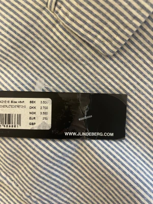 Randig kavaj från J.Lindeberg, oanvänd - Snygg kavaj från J.Lindeberg med smala blå och vita ränder. Tillverkad i ett exklusivt tyg från Angelico, Helt oanvänd med prislappen kvar, nypris 3 500 kr